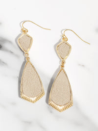Beige and gold earrings on a marble surface