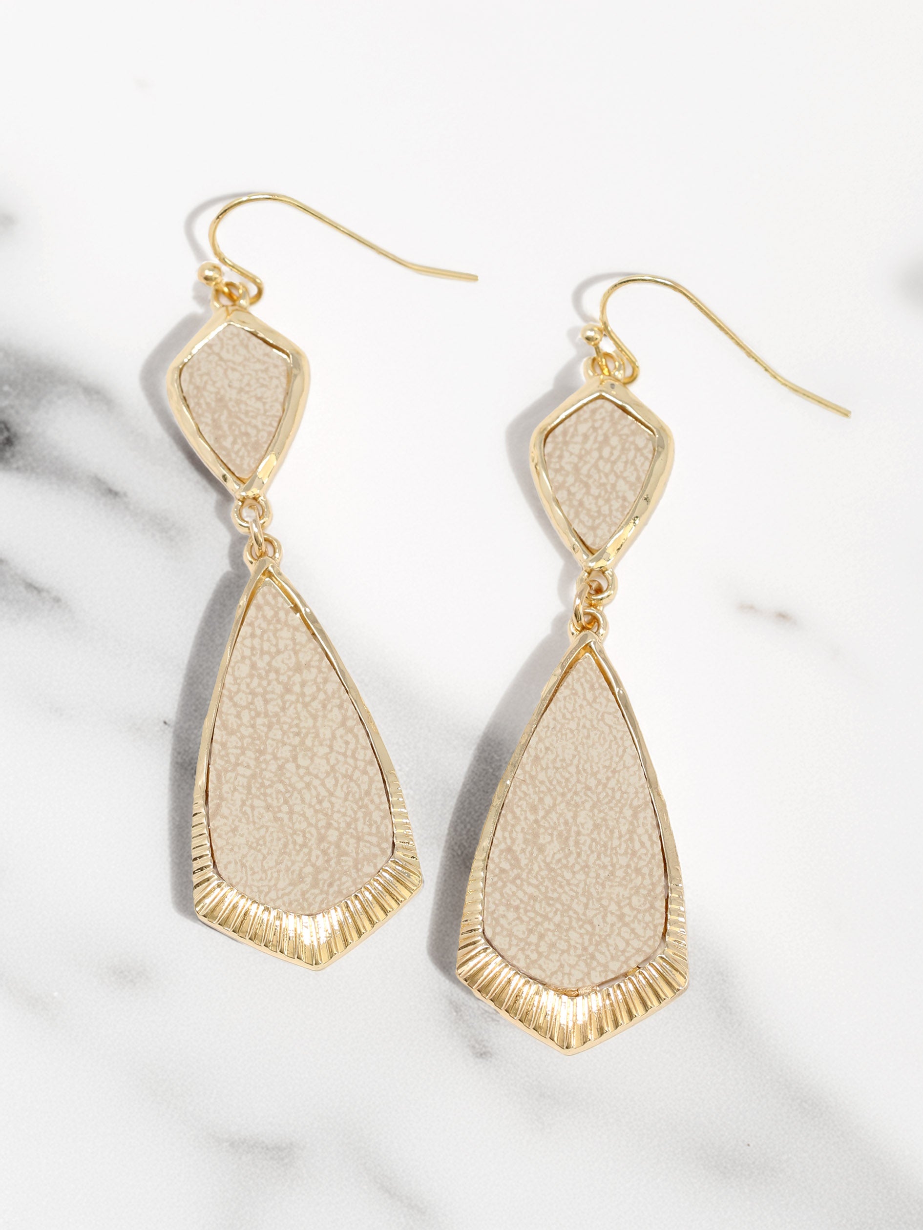 Beige and gold earrings on a marble surface