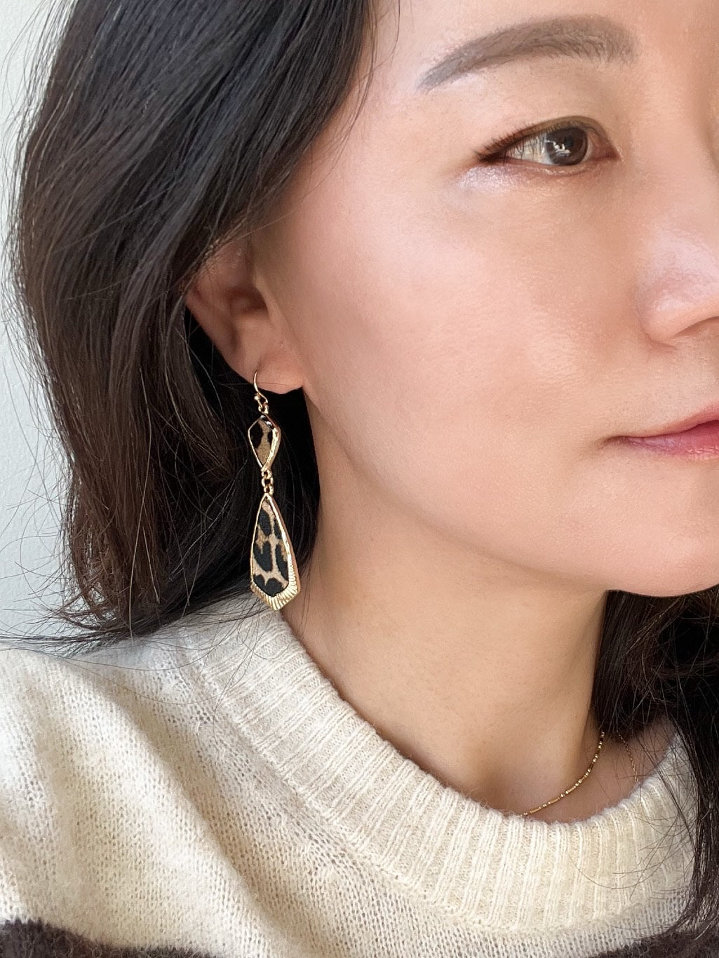 Close-up of a person wearing gold earrings with a white sweater.
