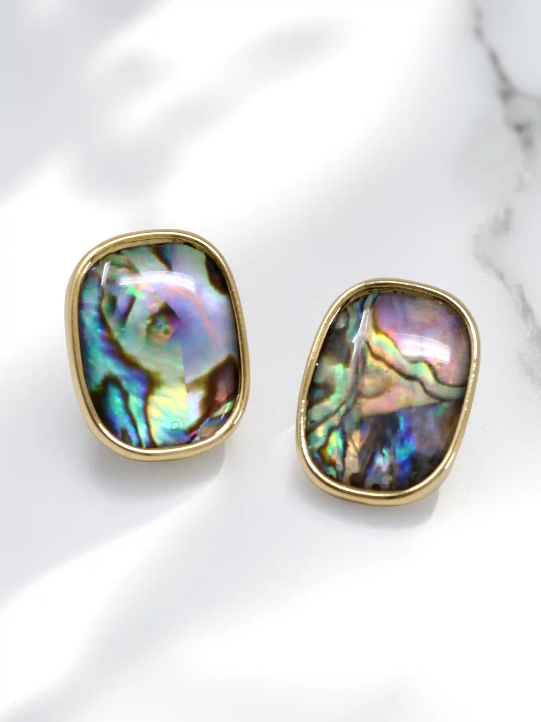 Pair of gold-framed abalone shell earrings on a white marble surface