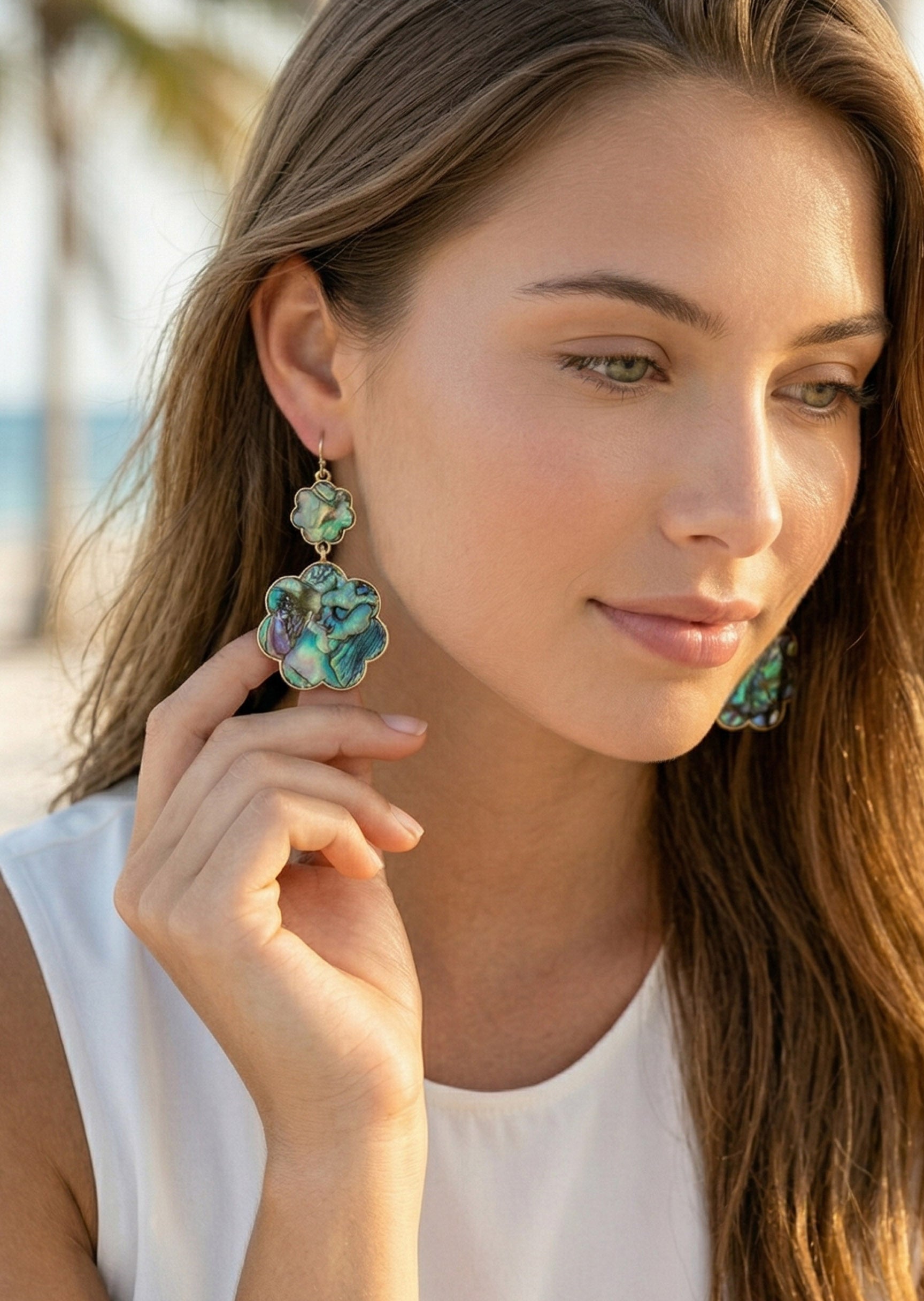 Woman wearing floral earrings with a blurred beach background