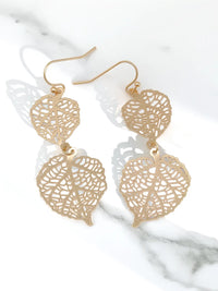 Gold leaf-shaped earrings on a marble surface