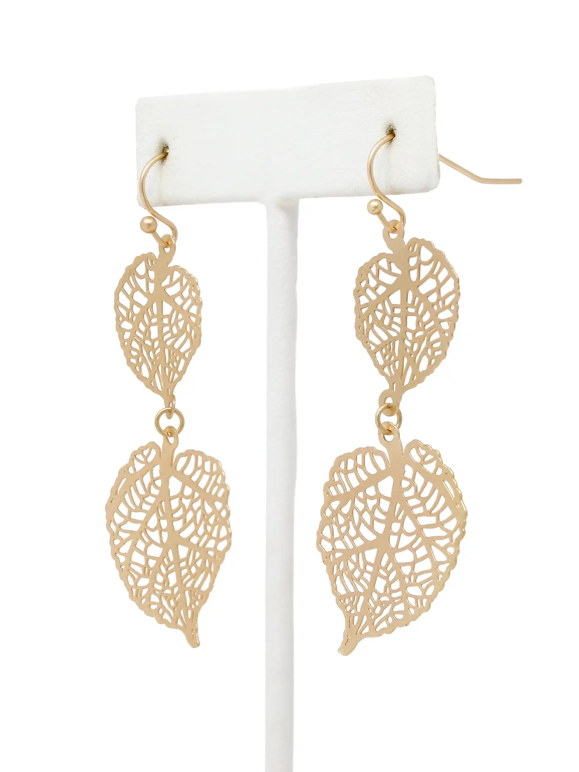 Gold leaf-shaped earrings on a white stand