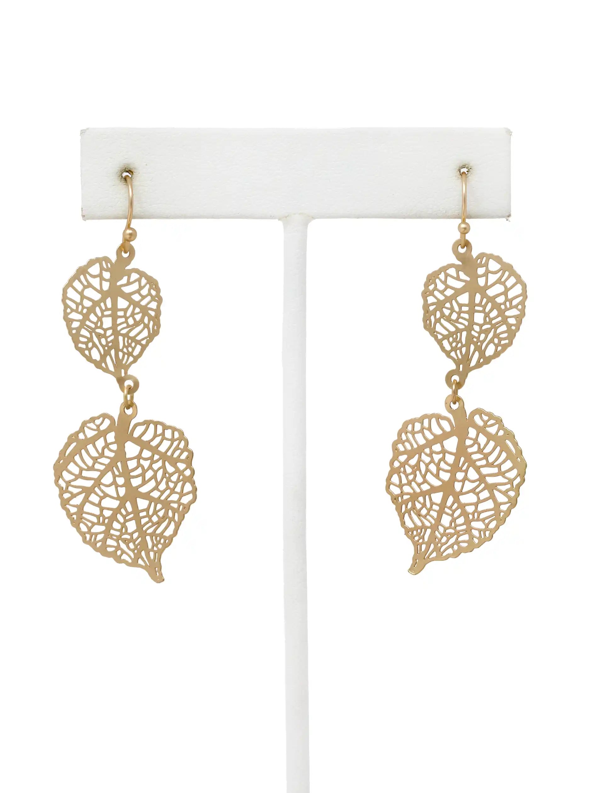 Gold leaf-shaped earrings on a white stand against a white background
