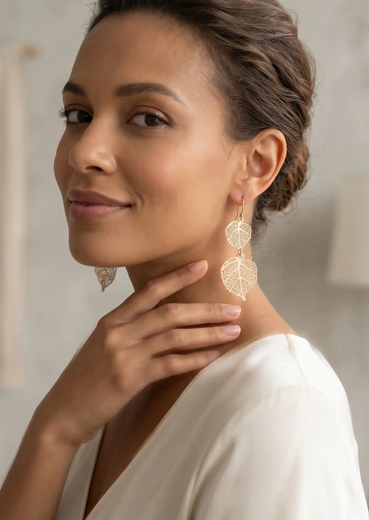 Woman wearing gold leaf earrings with a neutral background