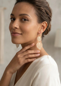 Woman wearing gold leaf earrings with a neutral background