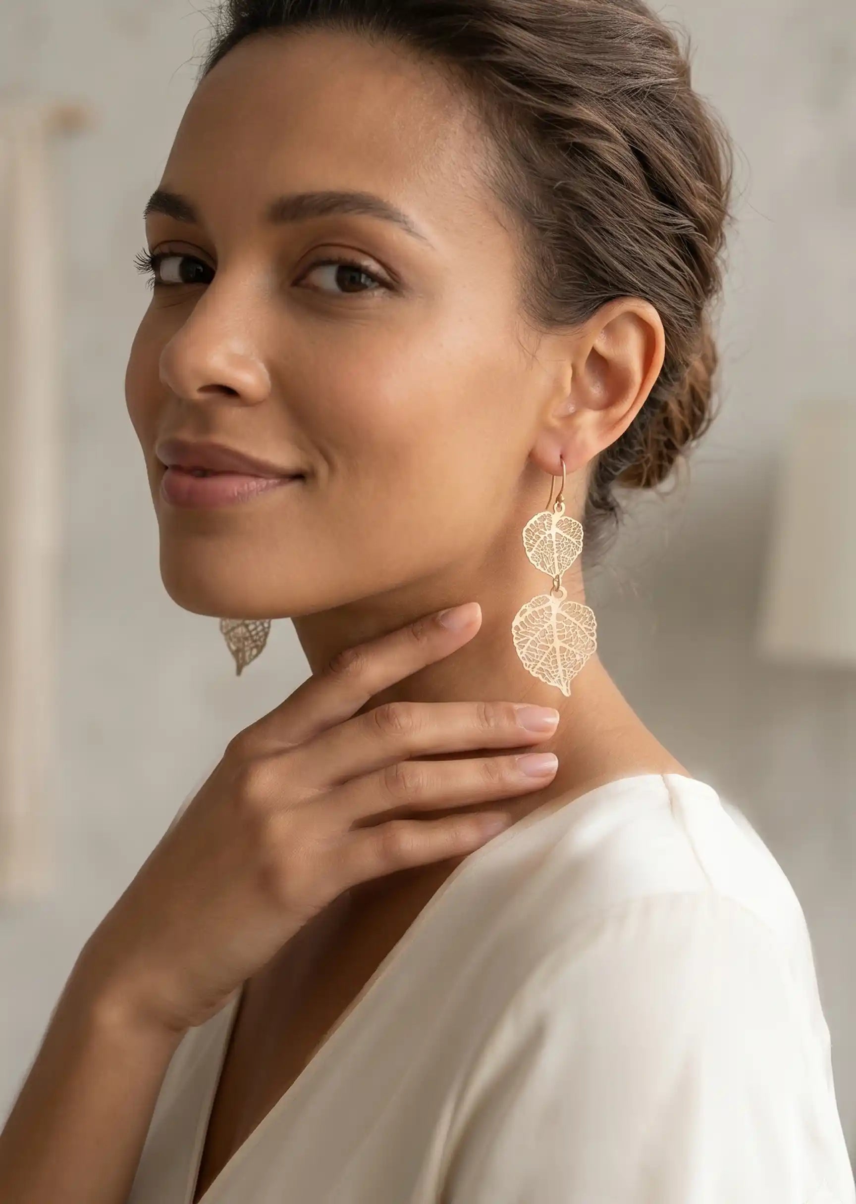 Woman wearing gold leaf earrings with a neutral background