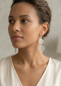 Woman wearing leaf-shaped earrings with a neutral background
