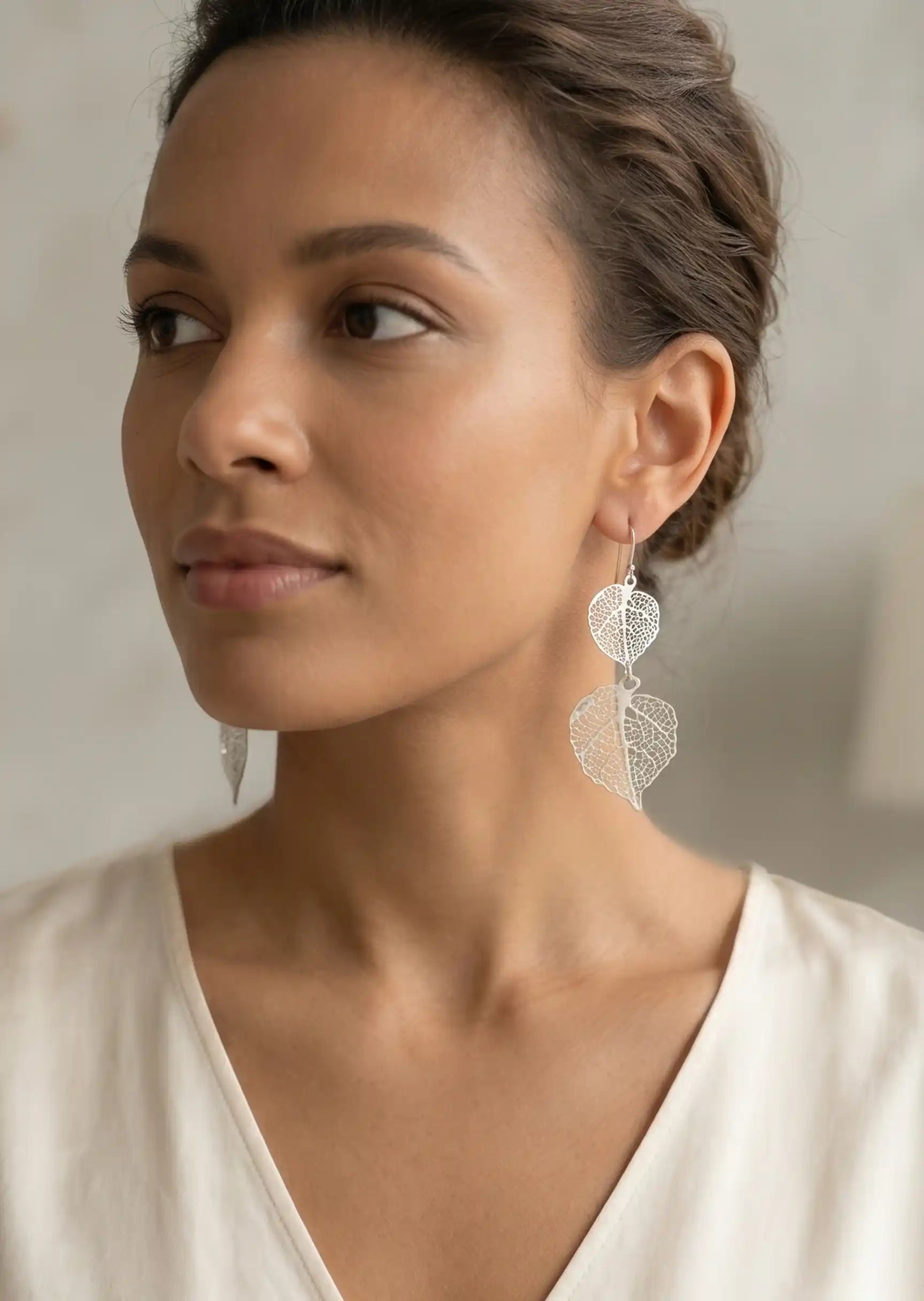 Woman wearing leaf-shaped earrings with a neutral background
