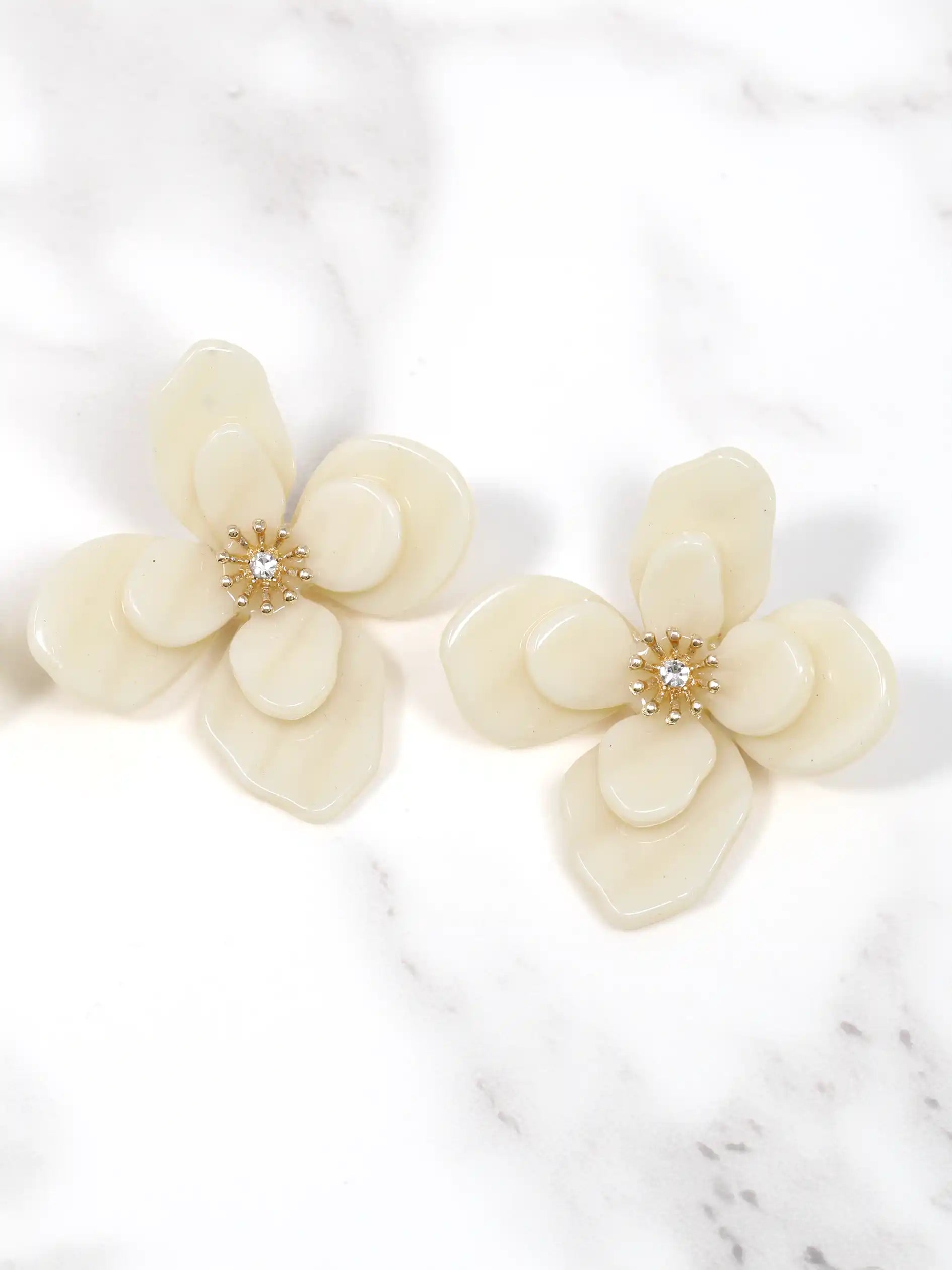 Cream-colored flower-shaped earrings on a marble surface