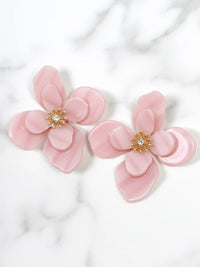 Pink flower-shaped earrings with a central gemstone on a white marble background