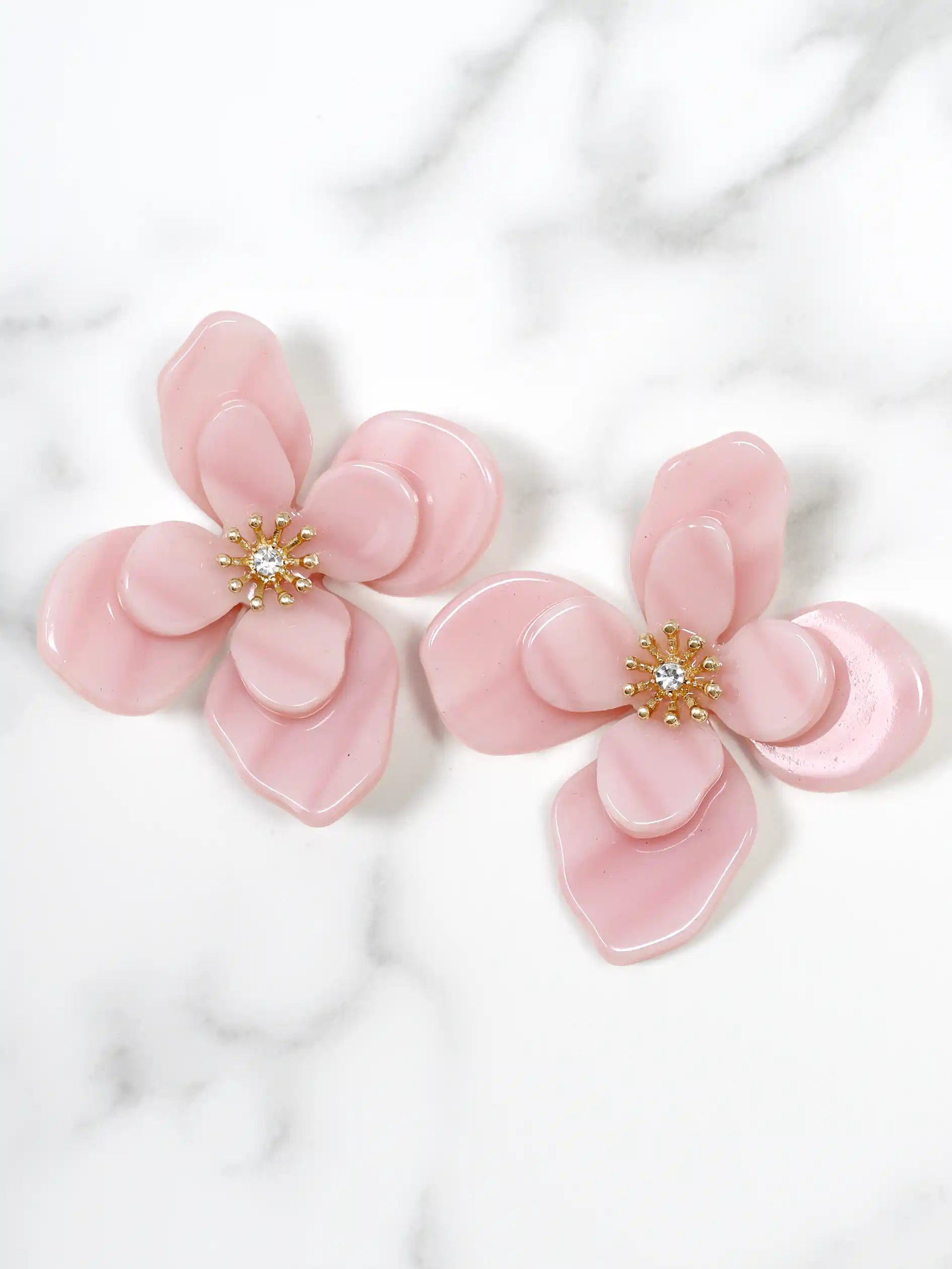 Pink flower-shaped earrings with a central gemstone on a white marble background