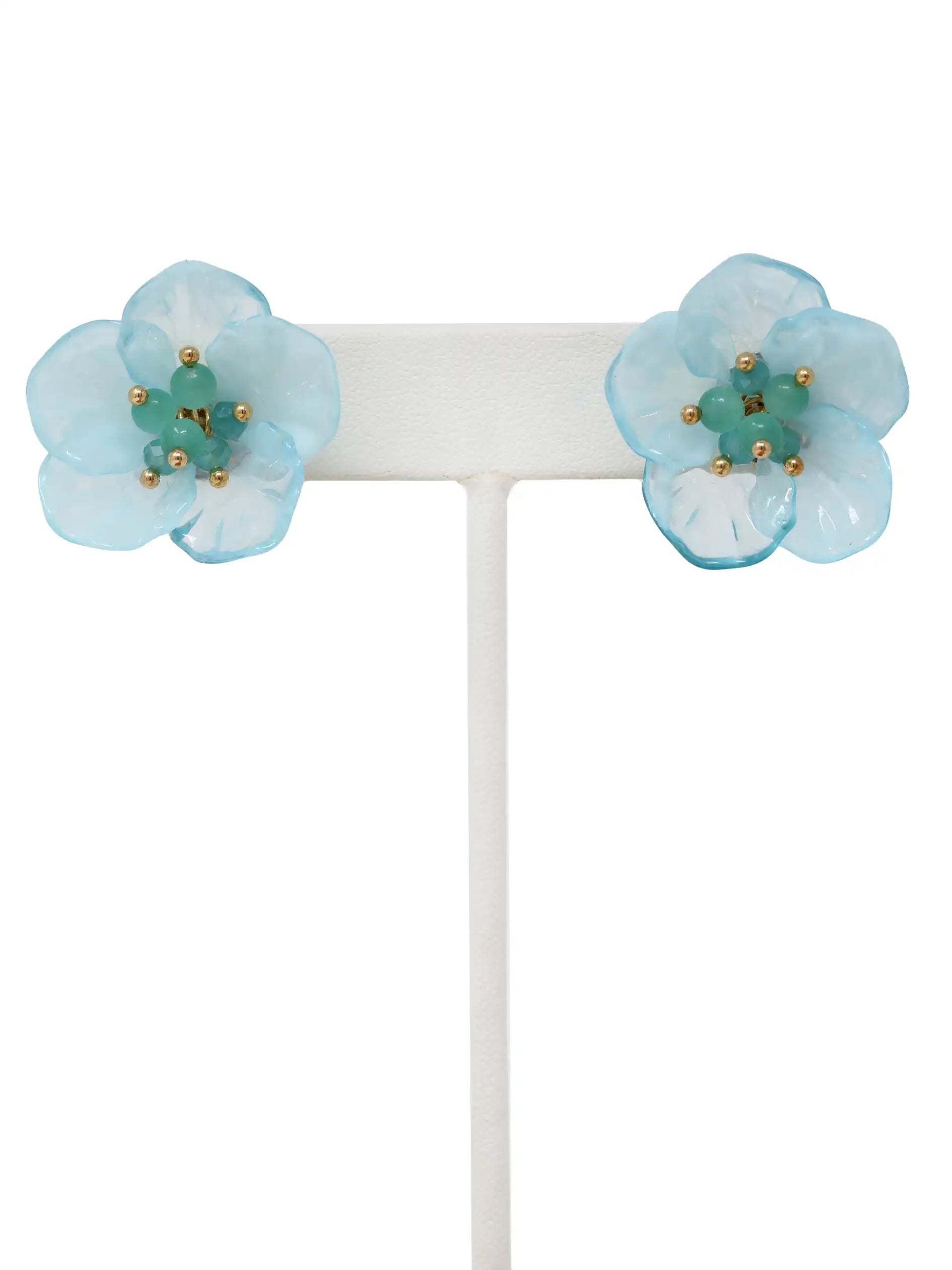 Light blue flower-shaped earrings on a white stand against a white background