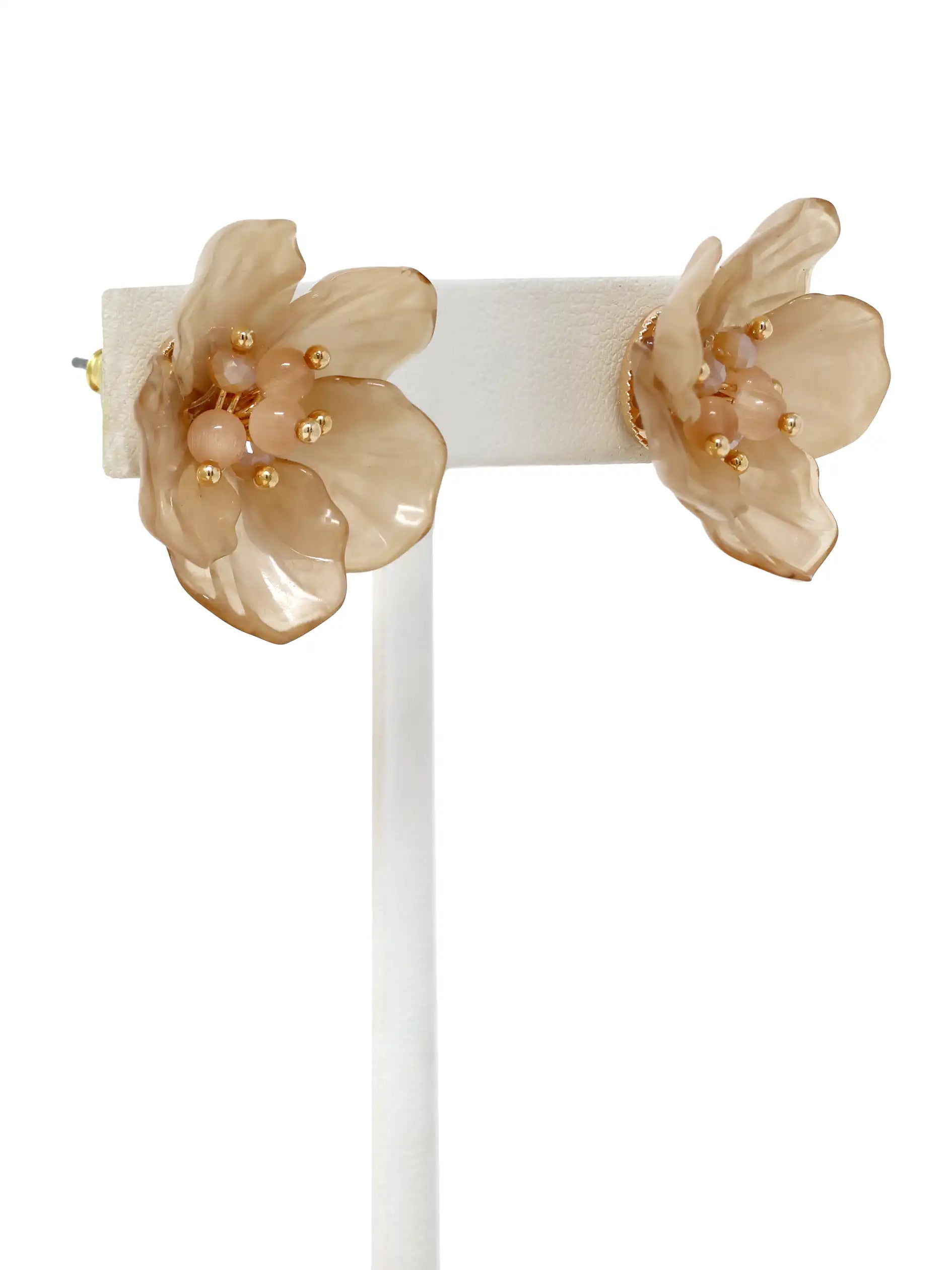 Pair of beige floral earrings on a white stand against a white background