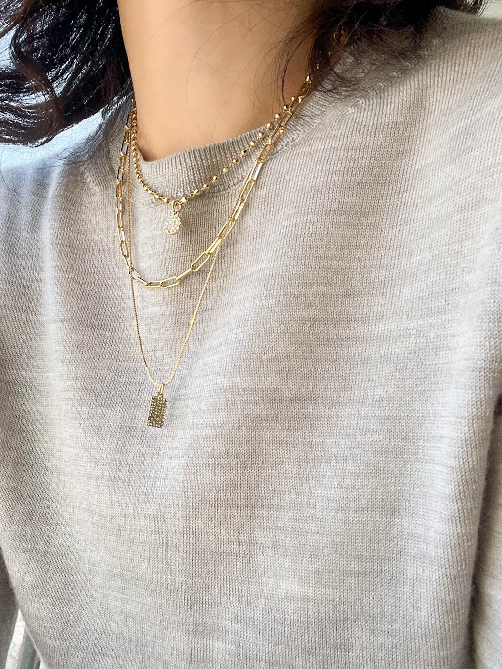 A triple-layered gold necklace featuring various chains adorned with modern, paved charms.