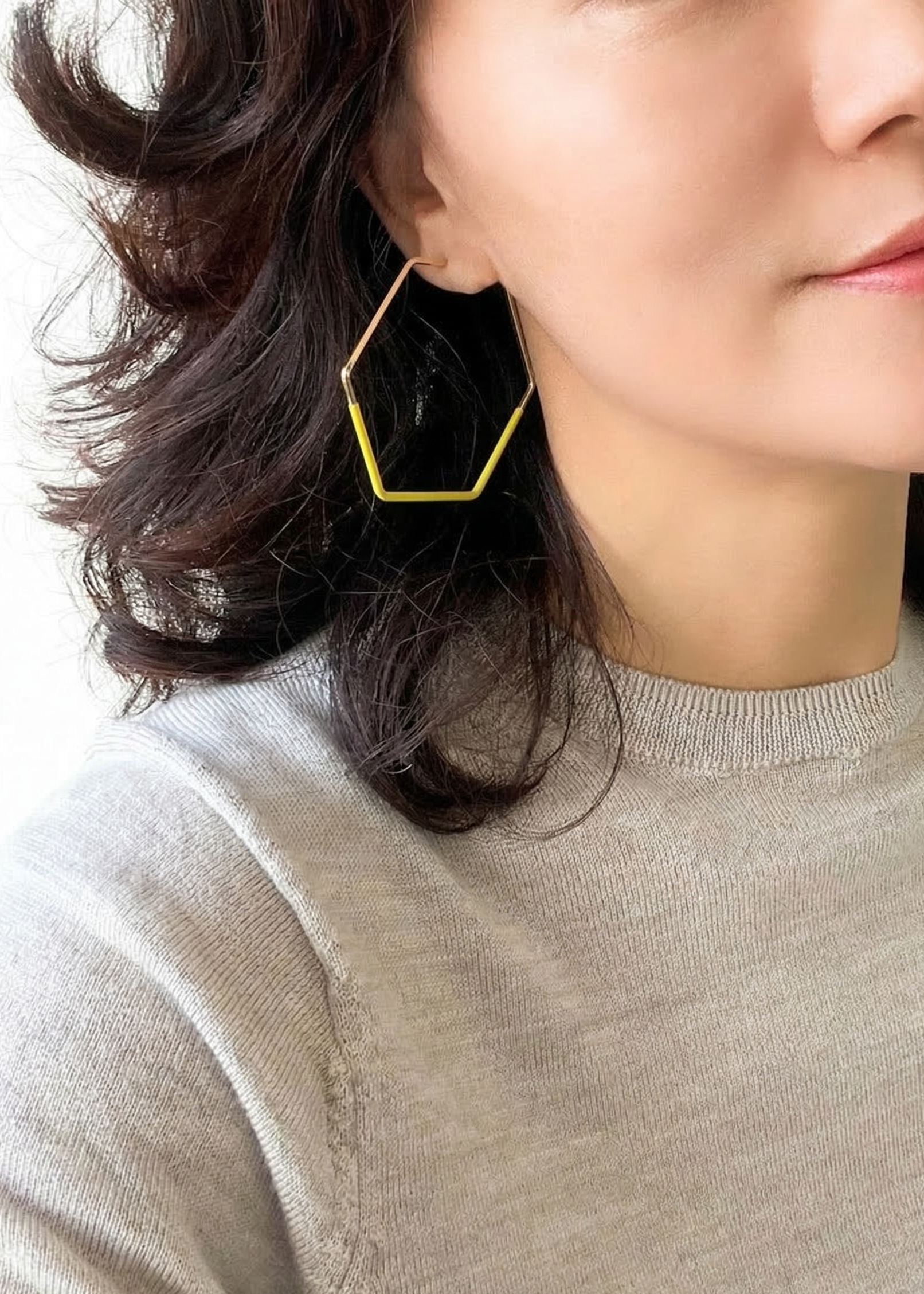Close-up of a person wearing a geometric gold earring against a neutral background