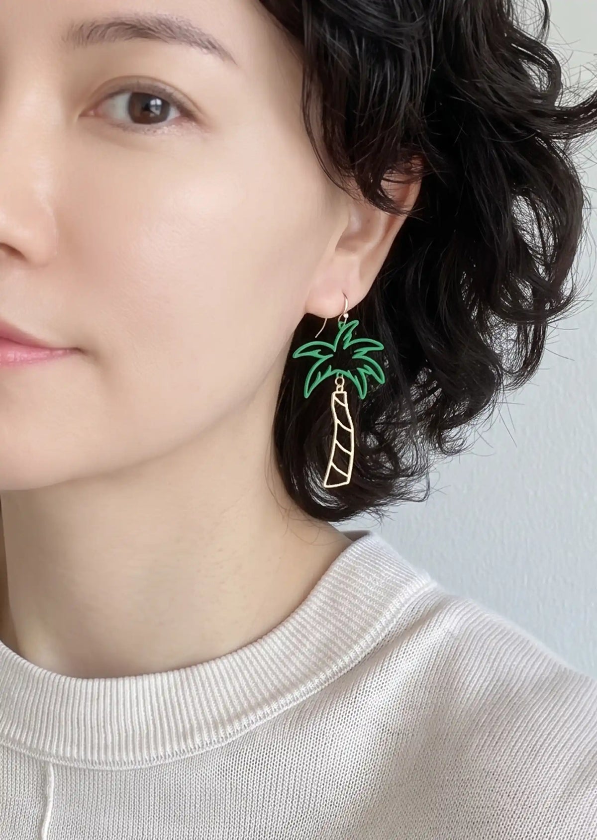 A pair of cutout palm tree drop earrings featuring bright green palm leaves and a gold-tone trunk, dangling from gold hook backings.