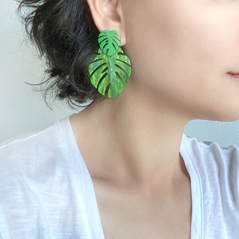 A woman wearing a pair of drop and dangle earrings featuring tropical green leaf resin, adding a vibrant touch to your style.