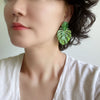 A woman wearing a pair of drop and dangle earrings featuring tropical green leaf resin, adding a vibrant touch to your style.