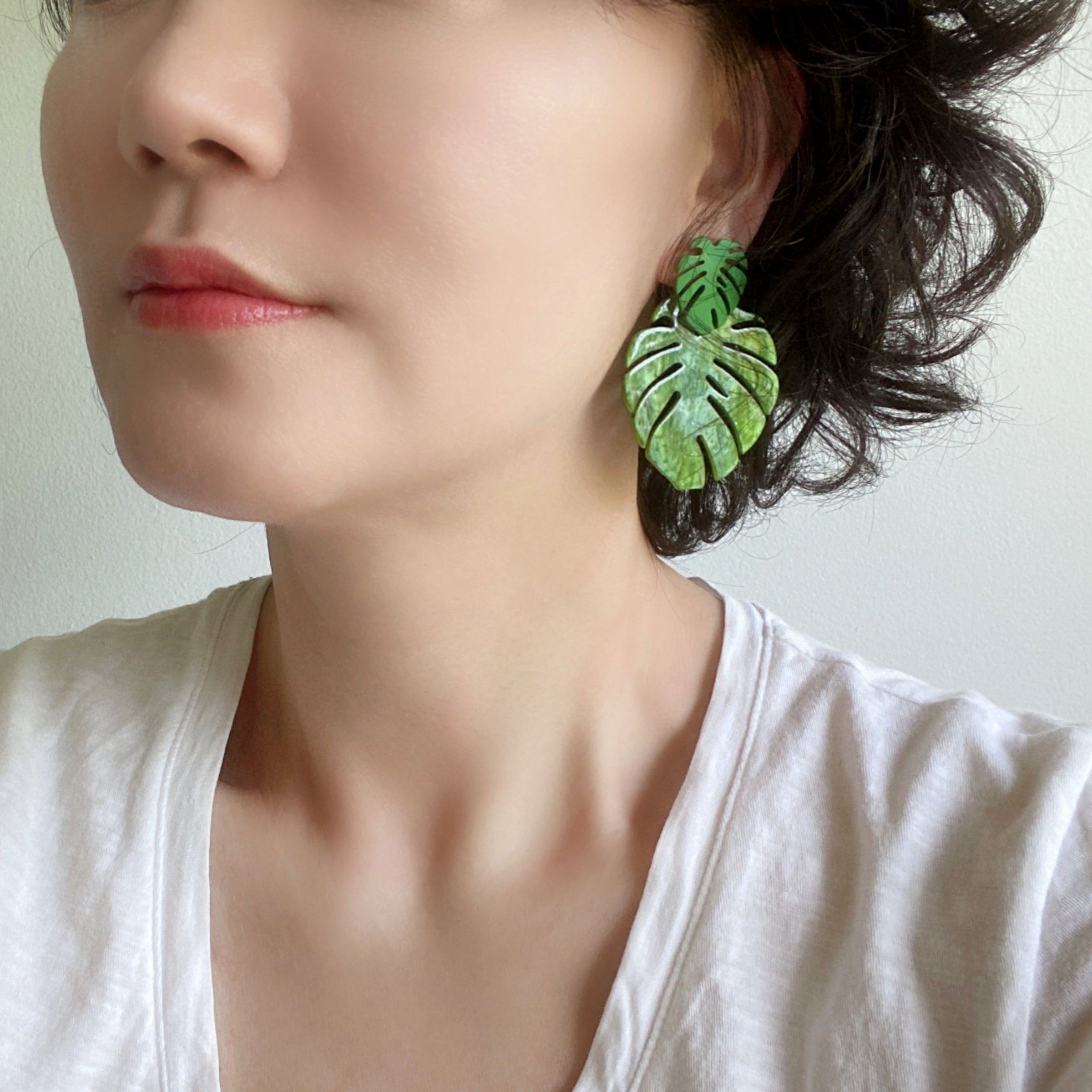 A woman wearing a pair of drop and dangle earrings featuring tropical green leaf resin, adding a vibrant touch to your style.