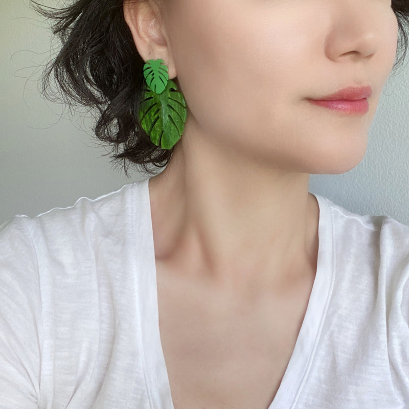 A woman wearing a pair of drop and dangle earrings featuring tropical green leaf resin, adding a vibrant touch to your style.