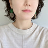 A woman wearing chic pineapple earrings with dangling design, showcasing green epoxy-coated tops resembling tropical leaves.