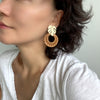 A pair of elegant circle rattan earrings with a decorative metal leaf accentuating the top.