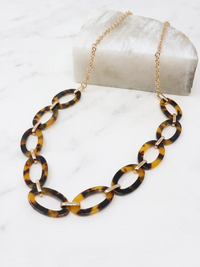 A gold-tone chain necklace featuring large, polished brown tortoise resin oval links, displayed on a white marble surface.