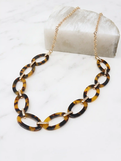 A gold-tone chain necklace featuring large, polished brown tortoise resin oval links, displayed on a white marble surface.