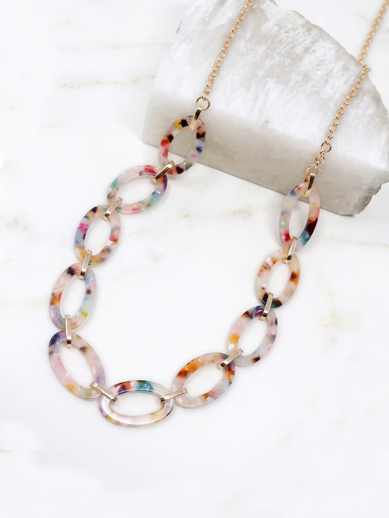 A multicolor marbled acrylic link necklace with gold-tone chain, displayed on a white marble surface with a white stone prop.