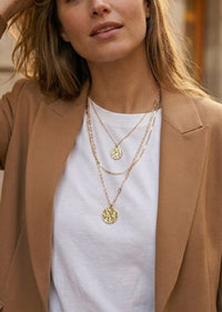 Woman wearing a brown blazer and white top with layered gold necklaces.