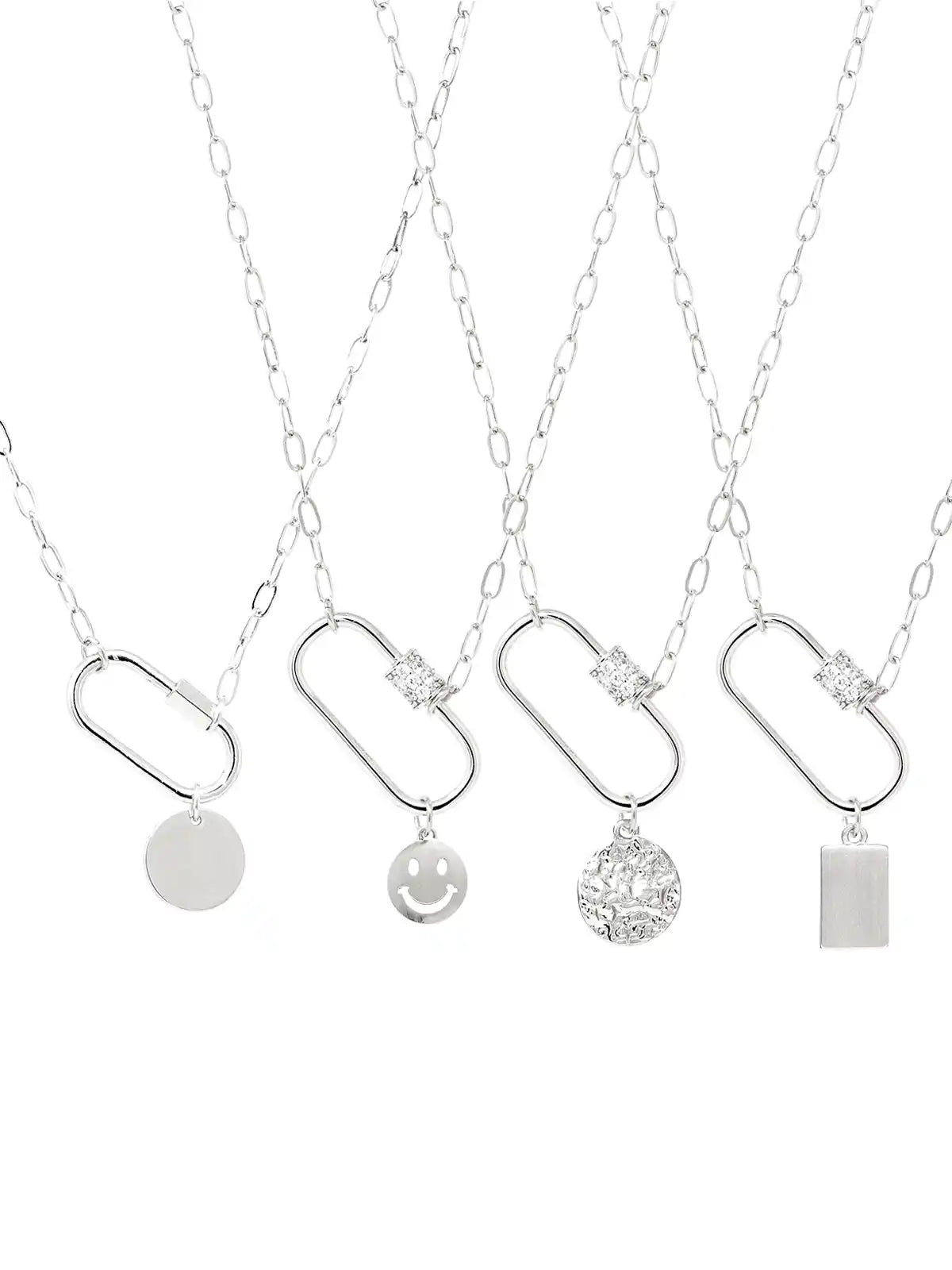 Four silver chain necklaces with capsule-shaped pendants and different dangling charms, including a smiley face, a textured round medallion, a blank round disc, and a rectangular block, displayed on a white background.