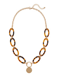 A statement necklace against a white background, featuring large, oval brown tortoise colored resin links connected by gold-toned metal and a central, polished gold-toned circular pendant.
