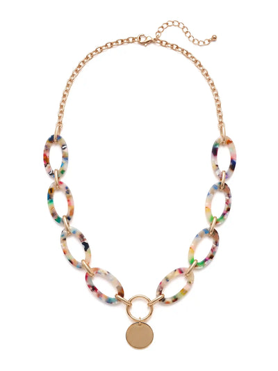A statement necklace against a white background, featuring large, oval multi colored resin links connected by gold-toned metal and a central, polished gold-toned circular pendant.