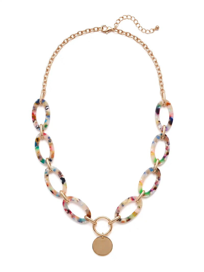 A statement necklace against a white background, featuring large, oval multi colored resin links connected by gold-toned metal and a central, polished gold-toned circular pendant.