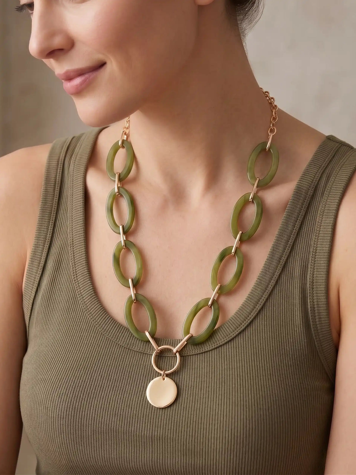 A statement necklace, featuring large, oval olive green colored resin links connected by gold-toned metal and a central, polished gold-toned circular pendant.