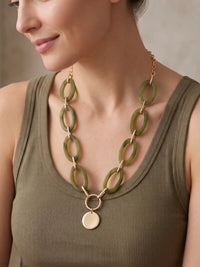 A statement necklace, featuring large, oval olive green colored resin links connected by gold-toned metal and a central, polished gold-toned circular pendant.