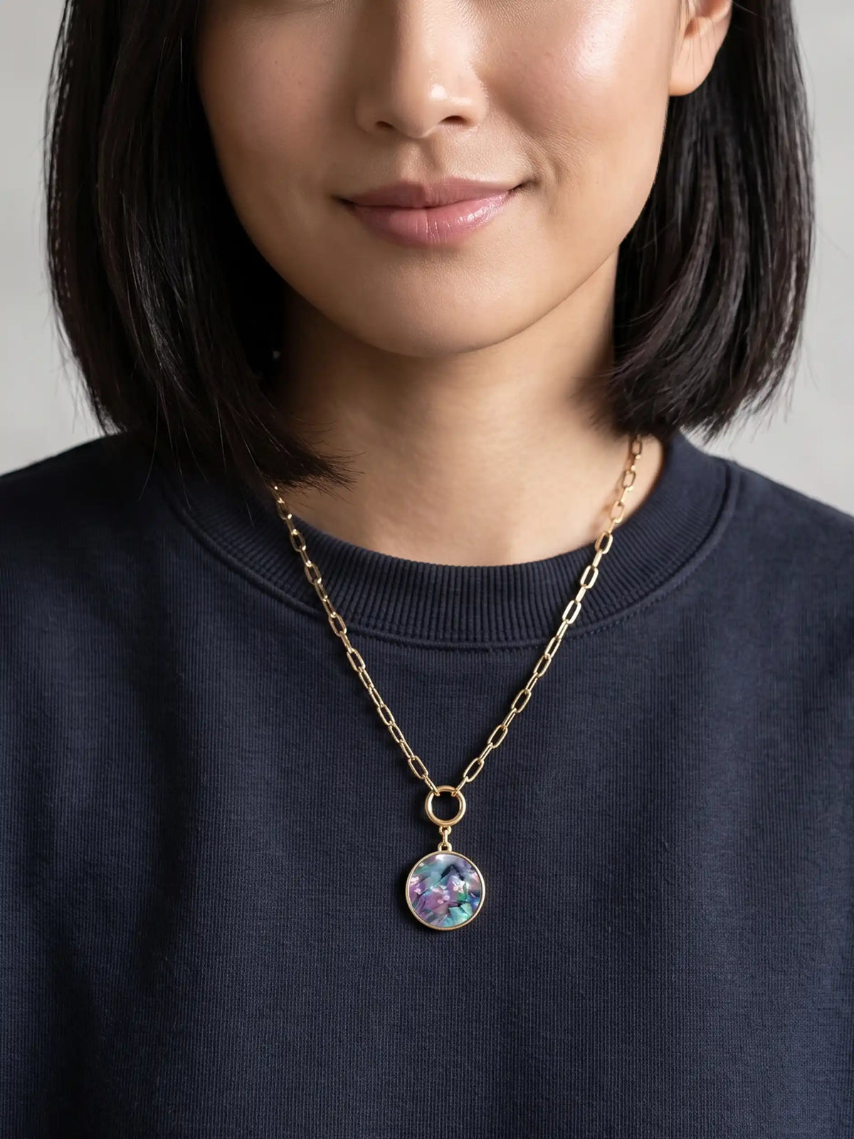 A close-up product image of the Modern Abalone Short Necklace, displaying a round, iridescent abalone shell pendant hanging from a gold-plated paperclip chain against a clean, light background.