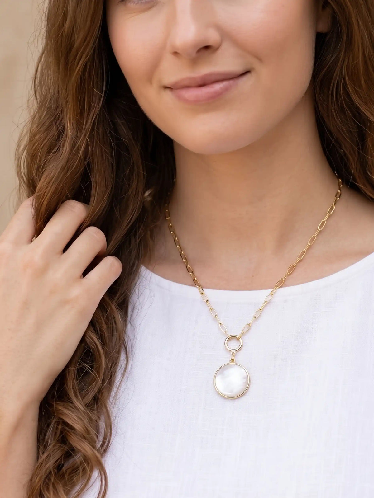 A close-up product image of the modern shell short necklace, displaying a round, iridescent mother of pearl shell pendant hanging from a gold-plated paperclip chain.