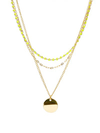A gold layered necklace featuring three distinct chains: a delicate chain with small lime green faceted beads, a chain with small gold links, and a longer chain with a polished gold disc pendant, set against a plain white background.