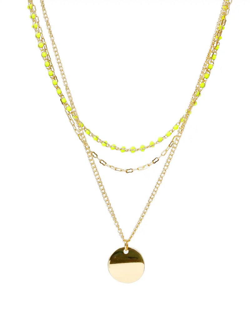 A gold layered necklace featuring three distinct chains: a delicate chain with small lime green faceted beads, a chain with small gold links, and a longer chain with a polished gold disc pendant, set against a plain white background.