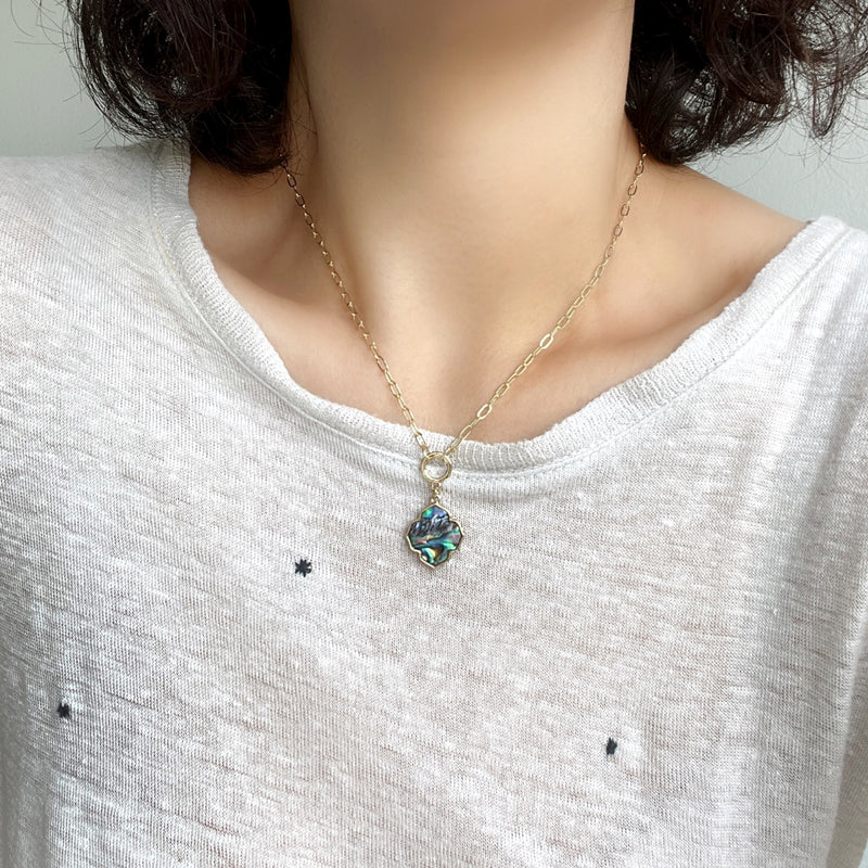 A short gold necklace featuring a natural abalone quatrefoil charm delicately dangled from a sleek and modern paperclip chain.