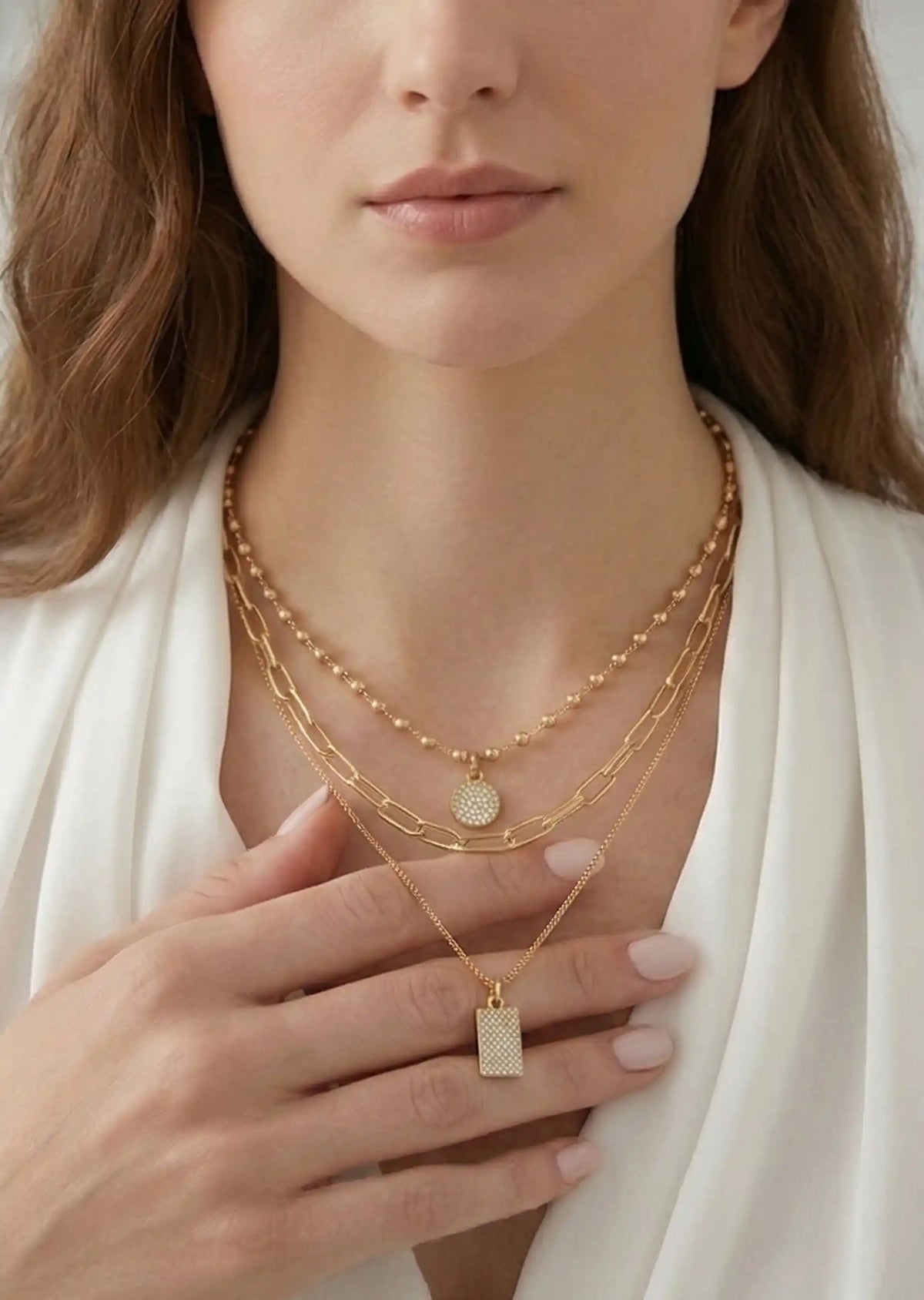 Close-up of a woman wearing multiple gold necklaces with a white top.