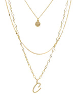 A three-layered gold necklace featuring a script initial charm and a small circle charm paved with stones.