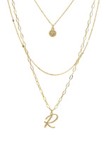 A three-layered gold necklace featuring a script initial charm and a small circle charm paved with stones.