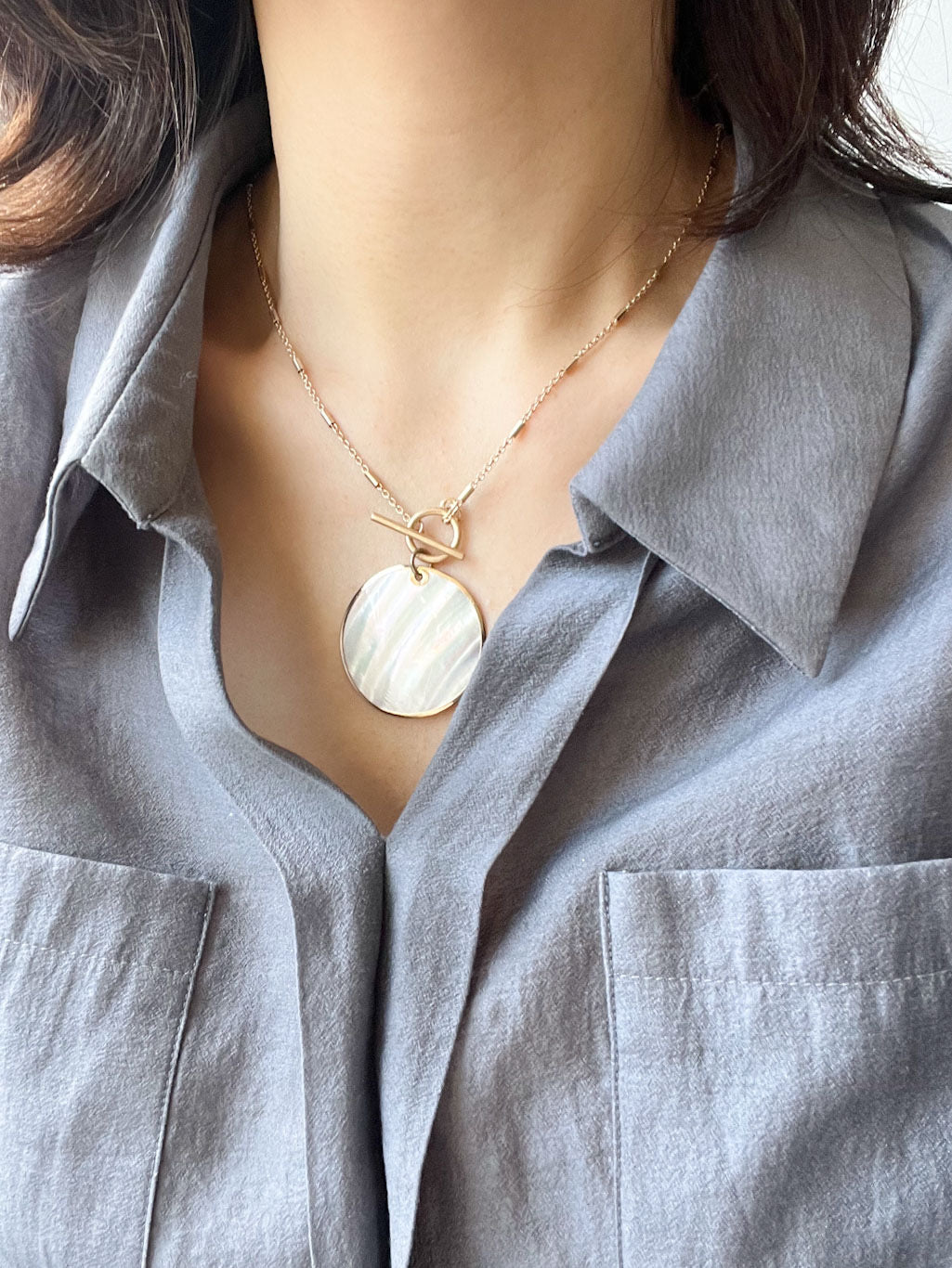 Gold chain necklace with a round Mother of Pearl shell pendant and toggle clasp closure.