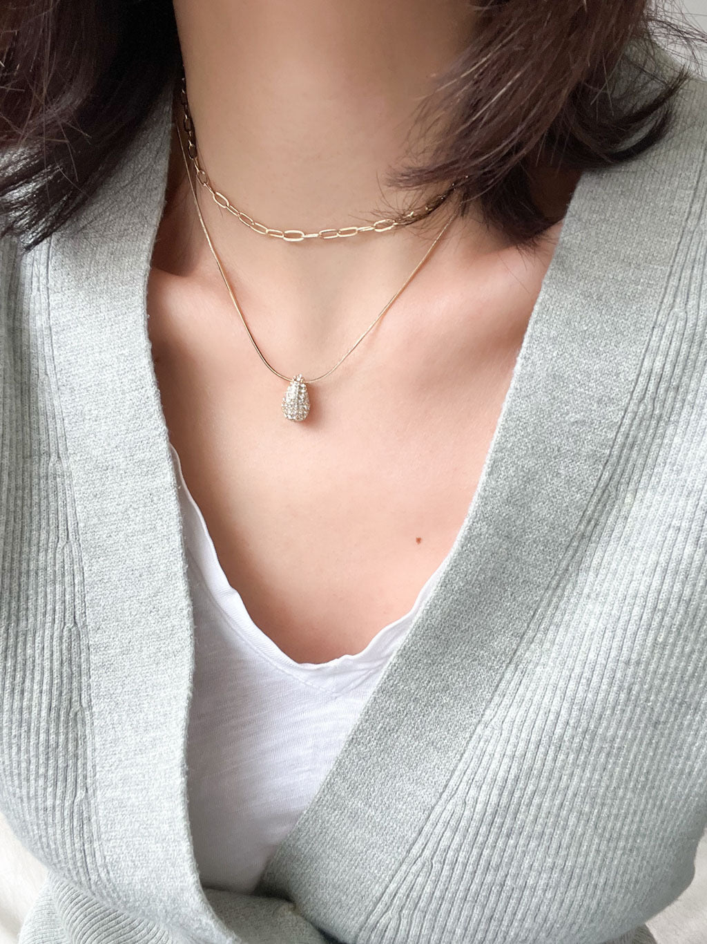 Gold double-layered necklace with a puffy crystal-paved teardrop charm, featuring a snake chain and a paperclip chain design.

