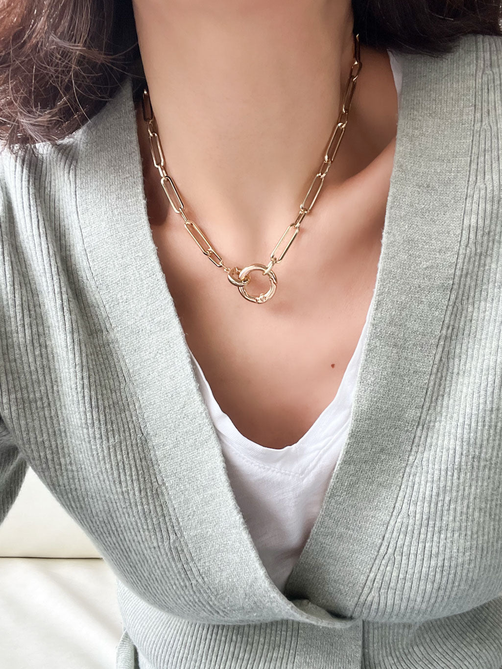Gold paperclip chain necklace with elongated rectangular links and a circular carabiner lock pendant in the center.