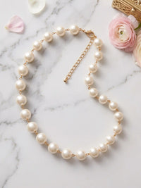 A delicate necklace featuring a strand of round, creamy white faux pearls. The pearls are strung on a fine gold-colored chain, with a matching clasp and adjustable extender. This elegant piece is suitable for various occasions.