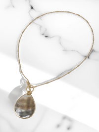 Gold necklace with a teardrop-shaped pendant on a marble surface